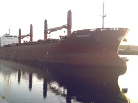 A bulk carrier moored at dusk, reflected in still water
