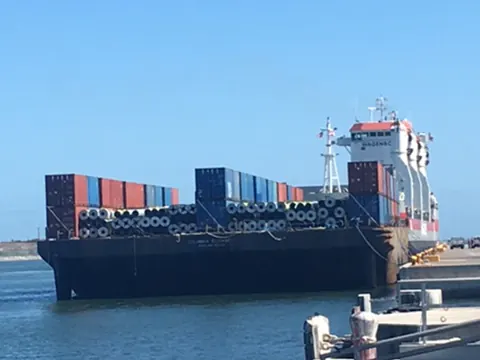 A barge loaded with shipping containers and steel cargo