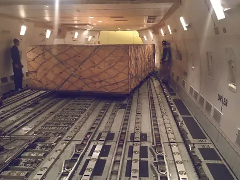 A netted crate on the rollers of a 747 main deck, two loaders beside it