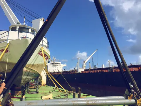A small vessel lashed on a ship's deck next to lifting gear