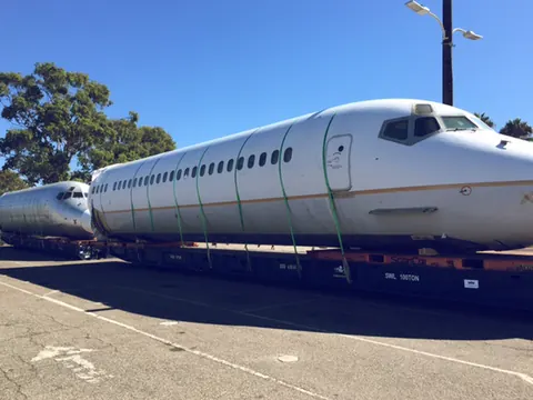 Two aircraft fuselage sections strapped to low trailers on a quay