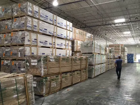 Packs of lumber stacked high in a warehouse, a man walking down the aisle