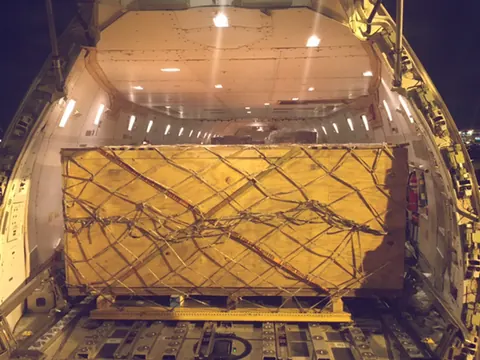 A large crate held down by nets inside a cargo plane
