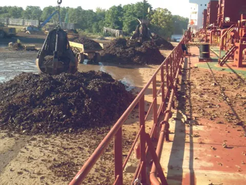Crane grabs loading scrap metal beside a ship