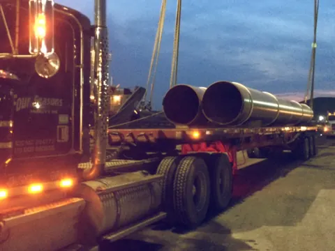 Large-diameter pipe on a flatbed truck at dusk